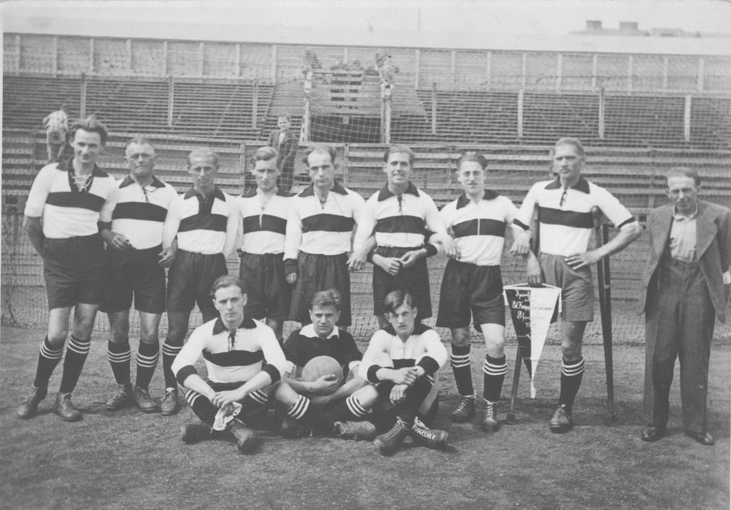 Die aus 11 Spieler bestehende Fußballmannschaft der Ersten österreichischen Krüppelarbeitsgemeinschaft in ihren neuen Trikots. Der Kapitän Wilfried Kobras (mit Krücken und einem Bein) hält den Vereinswimpel in der Hand.