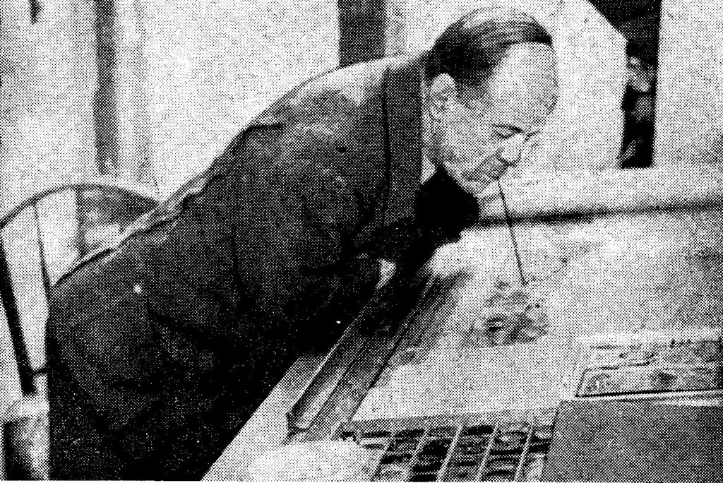 Der ca. 55-jährige Hans Susa, ohne Arme, malt ein Bild, gebeugt über den Tisch, mit dem Pinsel im Mund.