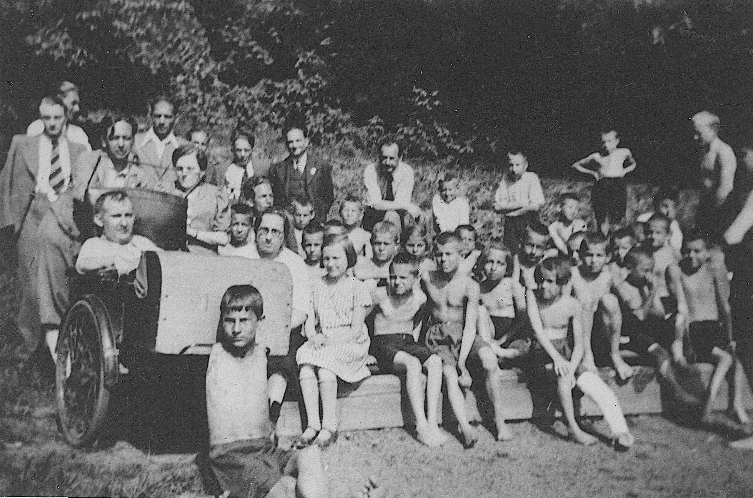 Siegfried Braun im Rollstuhl auf einem Gruppenbild mit vielen Kindern und ein paar Erwachsenen bei warmem Wetter in der Natur. Darauf auch František Bakule. Die Kinder sind mit und ohne sichtbare Behinderungen.